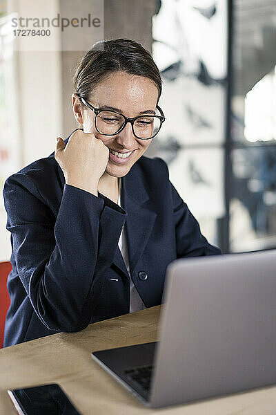 Lächelnde Geschäftsfrau  die einen Laptop benutzt  während sie im Büro sitzt