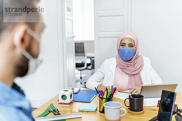 Frau mit Gesichtsmaske im Gespräch mit Mitarbeiterin im Büro sitzend