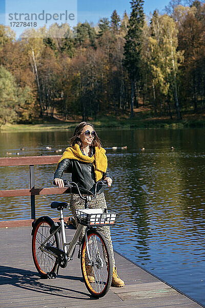 Frau mit Fahrrad auf dem Steg über dem See an einem sonnigen Tag