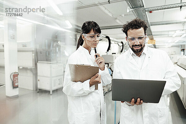 Lächelnder männlicher Wissenschaftler  der einen Laptop benutzt und neben einer Technikerin im Labor steht