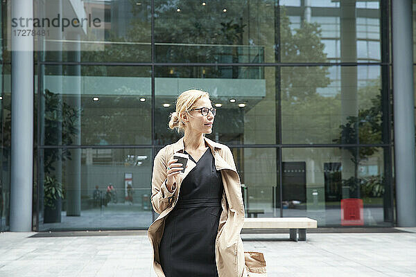 Frau hält Kaffeetasse  während sie vor einem Bürogebäude steht