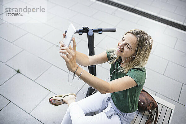 Mittlere erwachsene Frau  die ein Selfie macht  während sie auf einer Bank in der Stadt sitzt