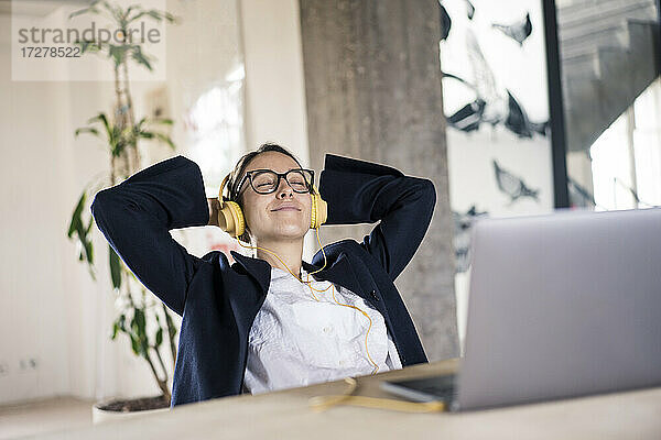 Lächelnde Geschäftsfrau hört Musik und entspannt sich auf einem Stuhl im Büro