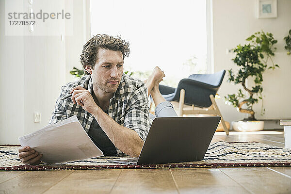 Mittelgroßer erwachsener Mann liegt auf der Vorderseite und benutzt einen Laptop zu Hause