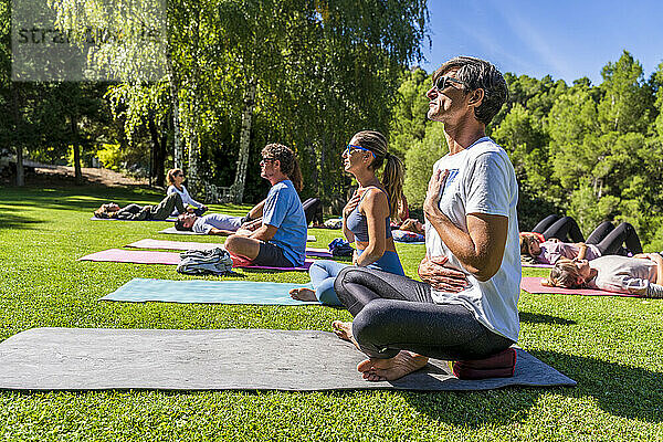 Ältere männliche und weibliche Touristen üben Yoga auf einer Matte in einem Gesundheitszentrum an einem sonnigen Tag