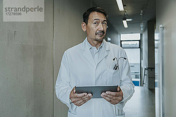 Wissenschaftler  der ein digitales Tablet benutzt  während er auf dem Klinikflur steht