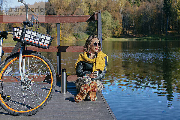 Frau trinkt Kaffee und entspannt sich auf einem Steg über dem See