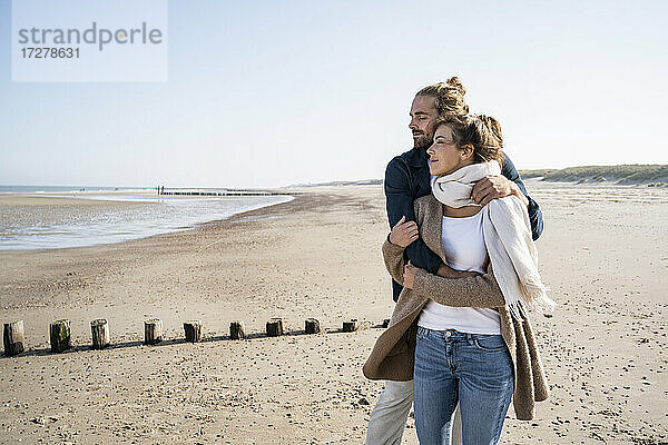 Junges Paar mit geschlossenen Augen umarmt  während am Strand gegen den klaren Himmel stehen