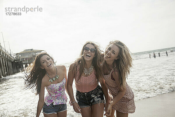 Fröhliche junge Freundinnen genießen das Wochenende am Strand bei klarem Himmel