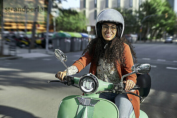 Lächelnde Frau auf einem elektrischen Motorroller in der Stadt an einem sonnigen Tag