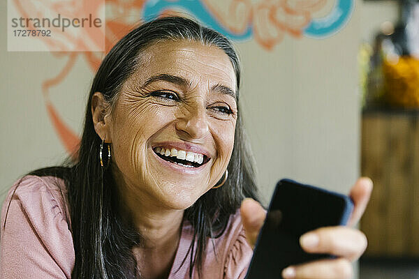 Fröhliche Frau hält ihr Smartphone  während sie an der Bar sitzt