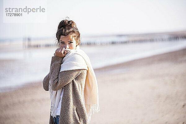 Schöne junge Frau steht am Strand an einem sonnigen Tag