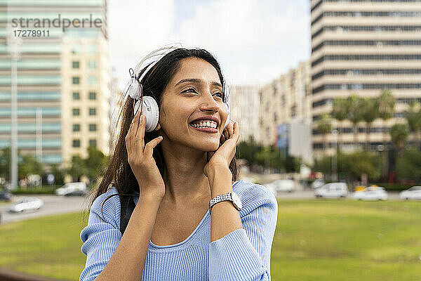Fröhliche junge Geschäftsfrau  die über Kopfhörer Musik hört  gegen die Stadt