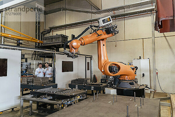 Geschäftsleute stehen vor einer automatischen Roboterarm-Maschine in einer Fabrik