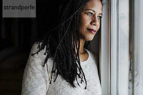 Nachdenkliche Frau  die durch ein Fenster schaut  während sie zu Hause steht