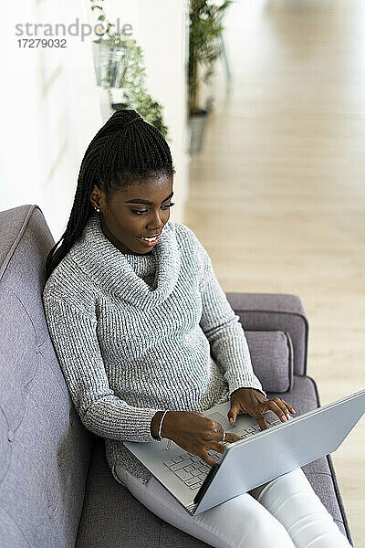 Junge Frau arbeitet am Laptop  während sie zu Hause im Wohnzimmer sitzt