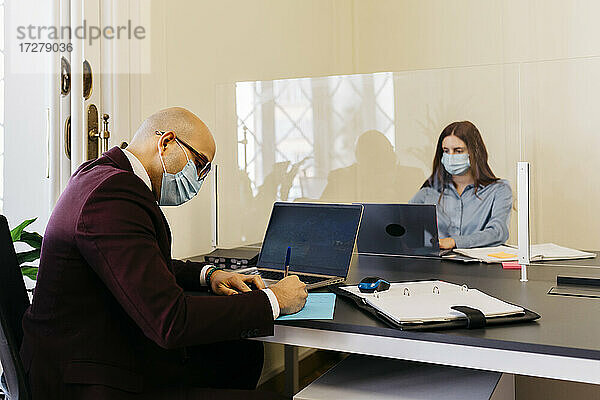 Männliche und weibliche Unternehmer mit Schutzmaske bei der Arbeit im Büro
