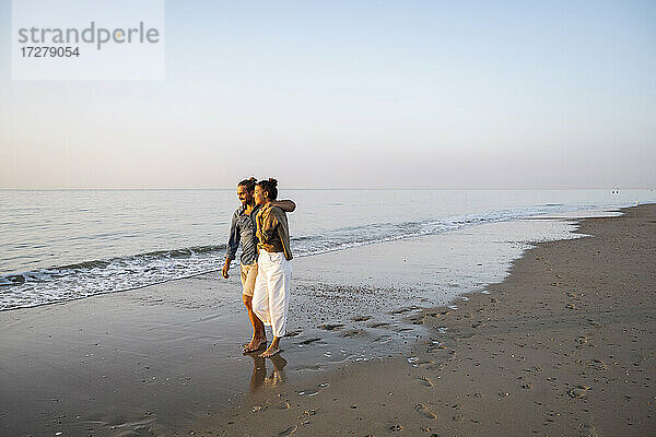 Lächelndes junges Paar genießt den Sonnenuntergang am Strand gegen den klaren Himmel