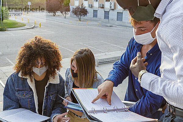 Männliche und weibliche Studenten tragen Schutzmasken  während sie auf dem Universitätscampus diskutieren
