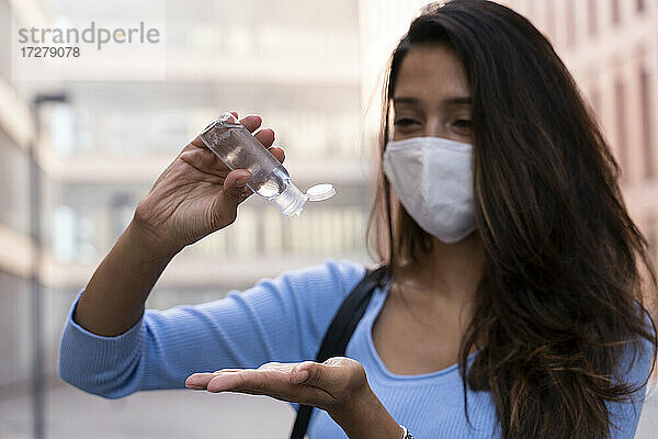 Geschäftsfrau mit Gesichtsmaske  die während der COVID-19 Desinfektionsmittel auf die Hand gießt