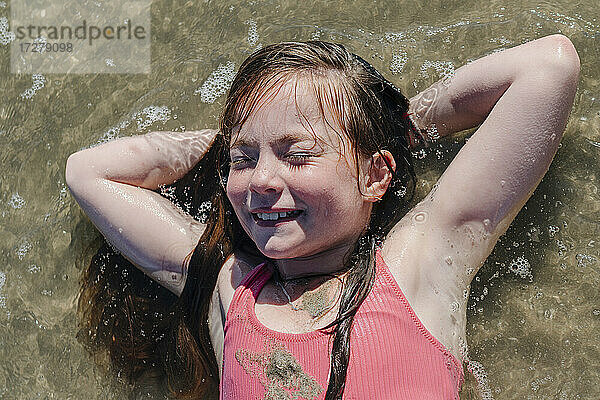 Mädchen auf dem Rücken liegend mit den Händen hinter dem Kopf im Wasser an einem sonnigen Tag