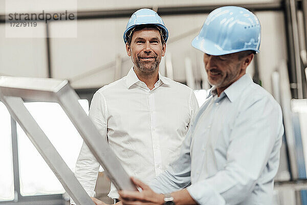 Männlicher Ingenieur lächelt  während sein Kollege einen Metallrahmen in der Industrie hält