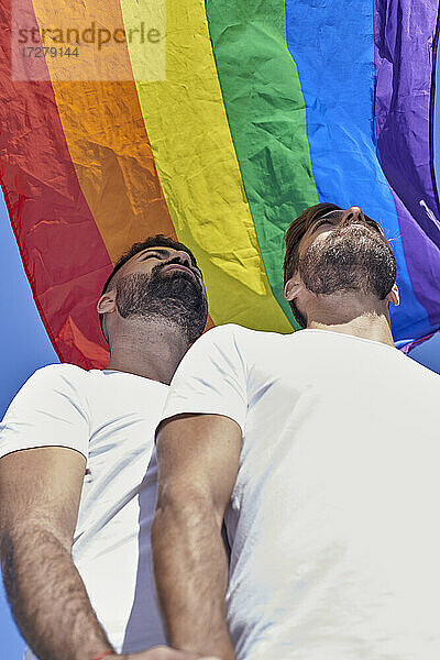 Schwules Paar schaut weg  während es unter der Regenbogenflagge steht