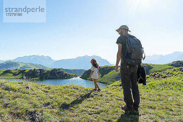 Vater und Tochter stehen auf einer Wiese und schauen auf einen See an einem sonnigen Tag