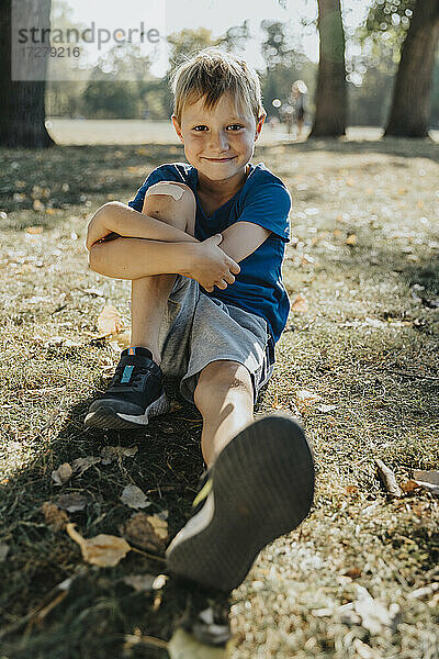 Lächelnder Junge sitzt im öffentlichen Park an einem sonnigen Tag