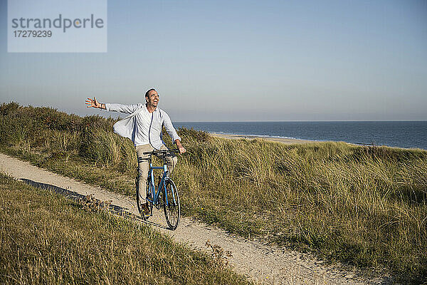 Unbeschwerter reifer Mann auf dem Fahrrad am Strand gegen den klaren Himmel am Wochenende