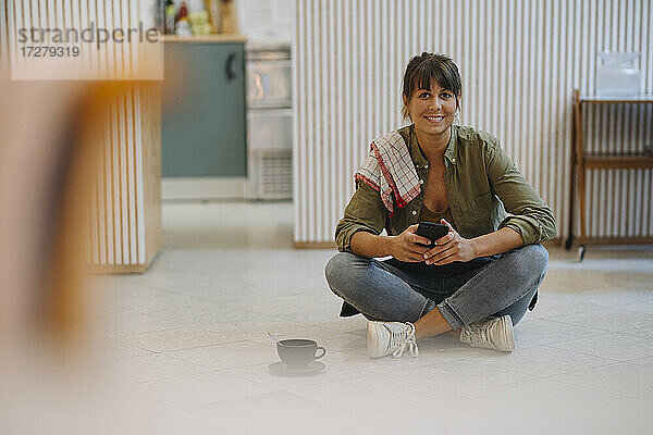 Lächelnde Geschäftsfrau  die ein Smartphone benutzt  während sie in einem Café auf dem Boden sitzt