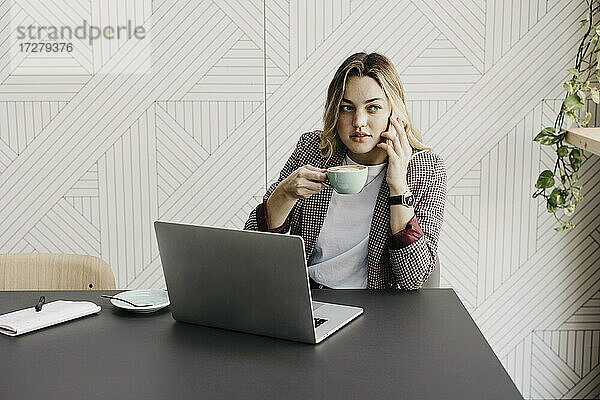 Junge Frau  die mit ihrem Smartphone telefoniert und Kaffee trinkt  während sie in einem Café sitzt