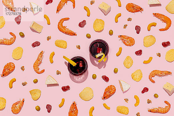 Wermutgetränk mit Garnelen  Käse  Herzmuscheln  Brotstangen  Kartoffelchips  Käsepuffs  Oliven und Wurst auf rosa Hintergrund