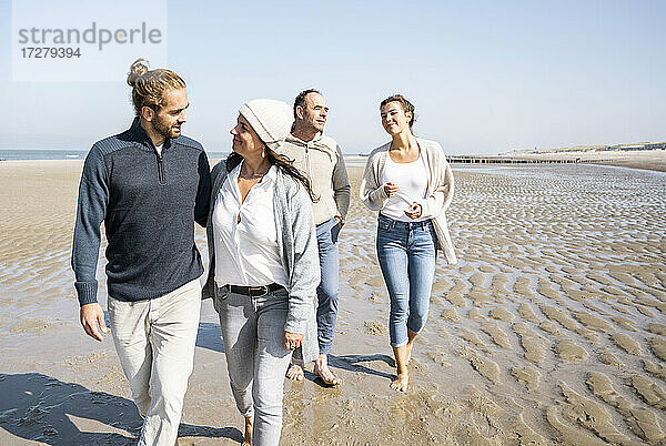 Mutter und Schwiegersohn im Gespräch beim Spaziergang mit Tochter und Vater im Hintergrund am Strand