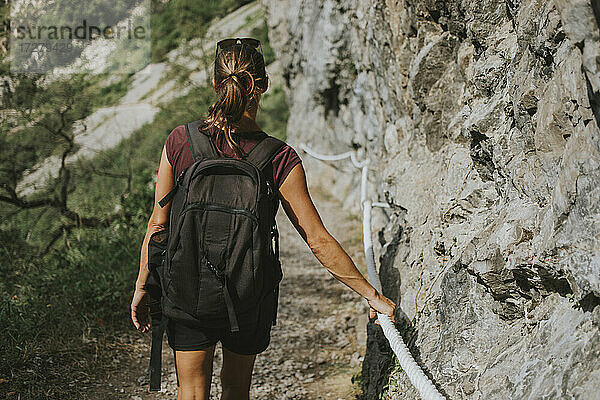 Wanderin mit Rucksack  die sich bergab bewegt  während sie ein Seil an einer Felsformation festhält