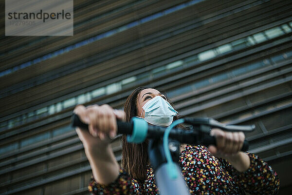 Ältere Frau mit Schutzmaske und Elektroroller vor einem Gebäude während der Coronavirus-Krise
