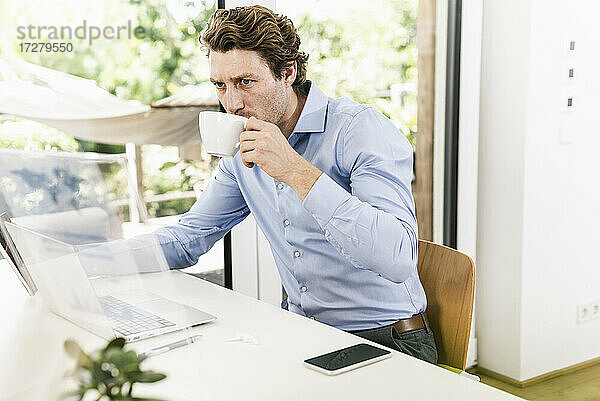 Mann arbeitet am Laptop und trinkt Kaffee im Büro