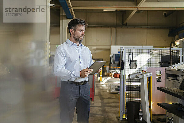 Geschäftsmann mit digitalem Tablet  der in einer Fabrik stehend Produktionsanlagen untersucht