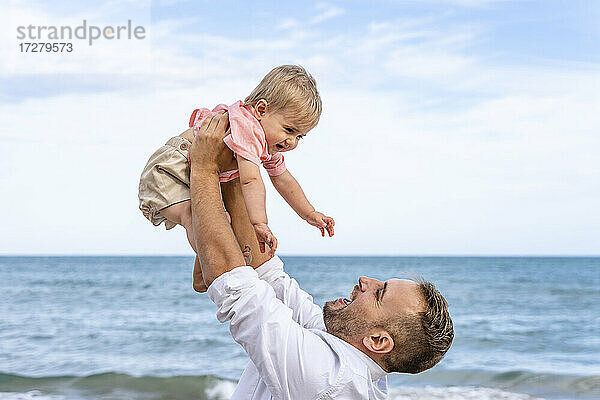 Lächelnder Vater  der seinen kleinen Jungen beim Spielen am Strand abholt