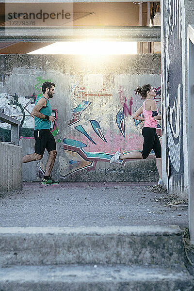 Aktives junges Paar joggt an Graffiti an der Wand vorbei