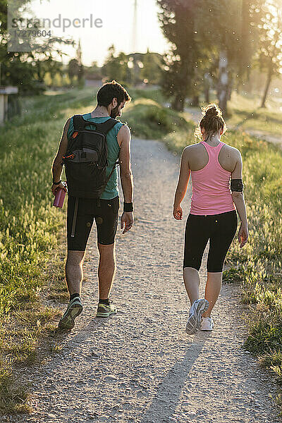 Aktives Paar in Sportkleidung beim Spaziergang im Park während des Sonnenuntergangs