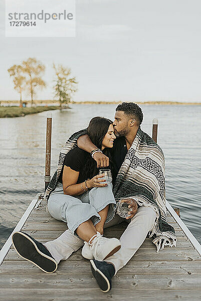 Mann küsst Frau  während er auf einem Steg am See sitzt