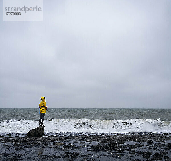 Frau steht auf einem Felsen am Meeresufer vor bewölktem Himmel