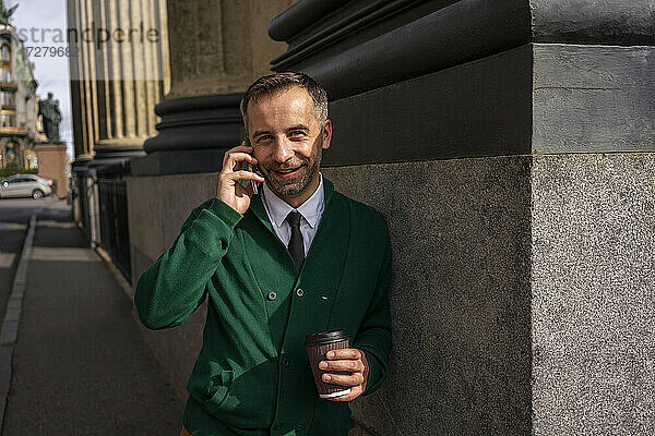 Lächelnder Geschäftsmann  der mit seinem Handy telefoniert und sich an eine Säule der Kasaner Kathedrale in Sankt Petersburg  Russland  lehnt
