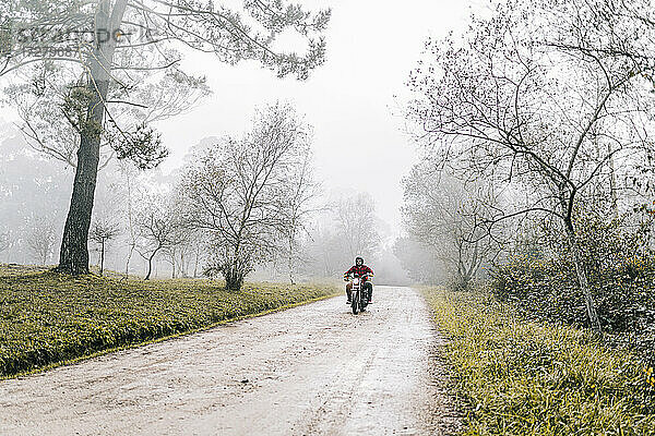 Mann fährt Motorrad auf unbefestigtem Weg bei nebligem Wetter