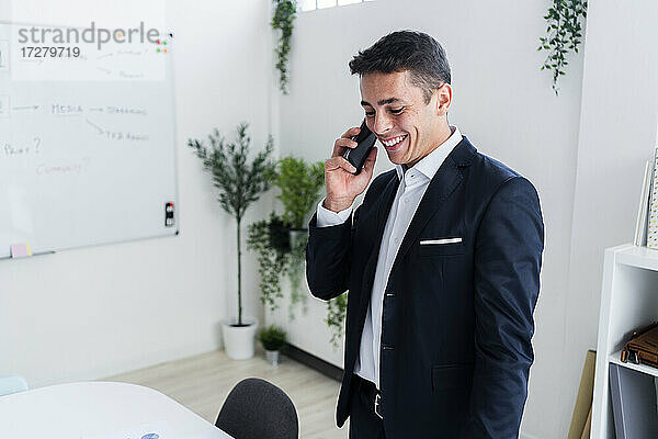 Lächelnder Geschäftsmann  der mit seinem Handy telefoniert  während er im Kreativbüro arbeitet
