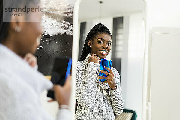 Lächelnde Frau nimmt Selfie durch Spiegelreflexion zu Hause
