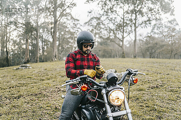 Männlicher Motorradfahrer trägt Handschuhe  während er im Wald auf dem Motorrad sitzt