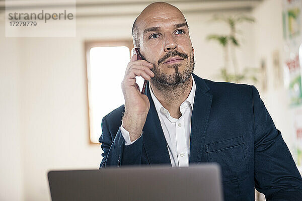 Geschäftsmann  der mit seinem Handy telefoniert  während er im Büro am Laptop arbeitet