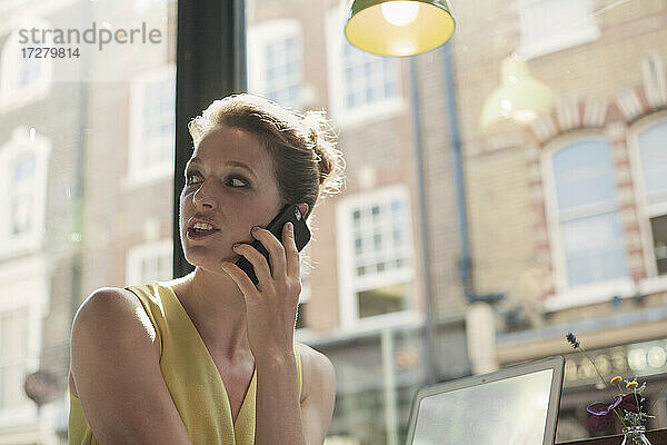 Junge Geschäftsfrau  die in einem Café mit einem Mobiltelefon spricht